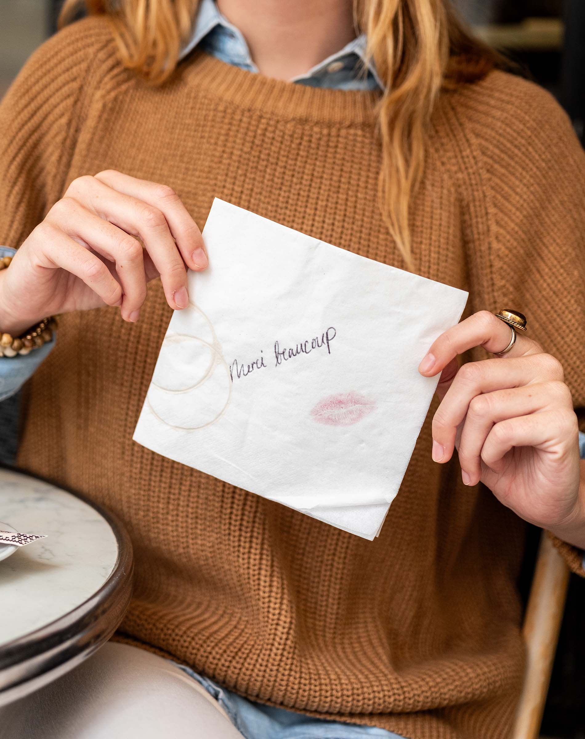 Person holding a white card with text and a lipstick mark, sitting at a table.