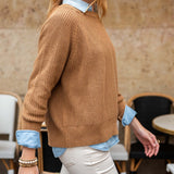 Woman wearing a brown sweater with rolled-up sleeves and white pants in an indoor setting.