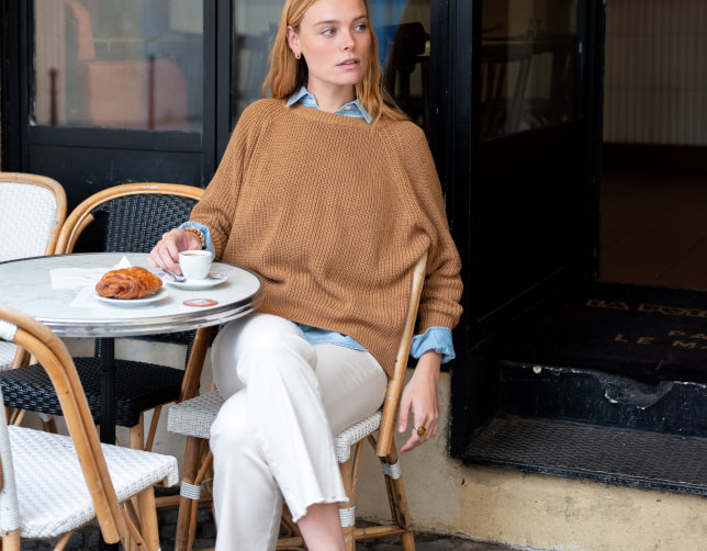 Image of a woman wearing a light brown knit sweater sitting at a cafe table