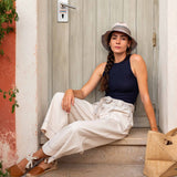 Woman sitting on steps wearing a hat and casual outfit with a bag next to her.