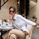 Woman sitting at an outdoor cafe wearing a white shirt and beige pants.