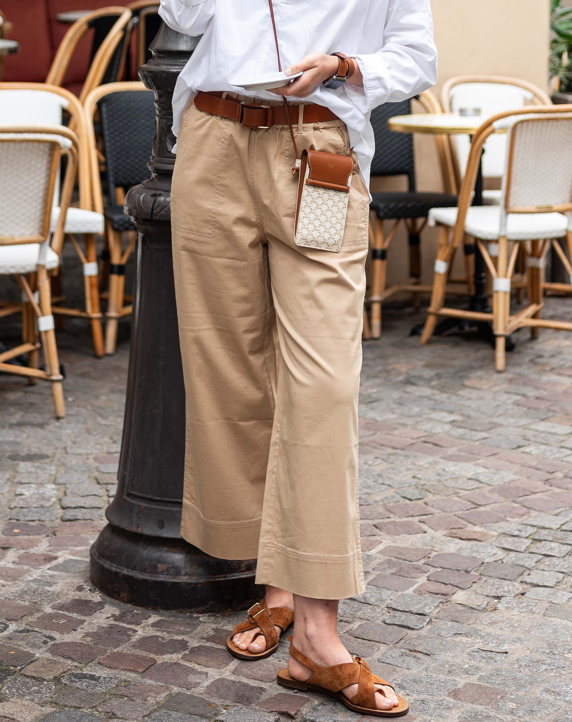Person wearing a white shirt, beige pants, and brown sandals in an outdoor cafe setting.