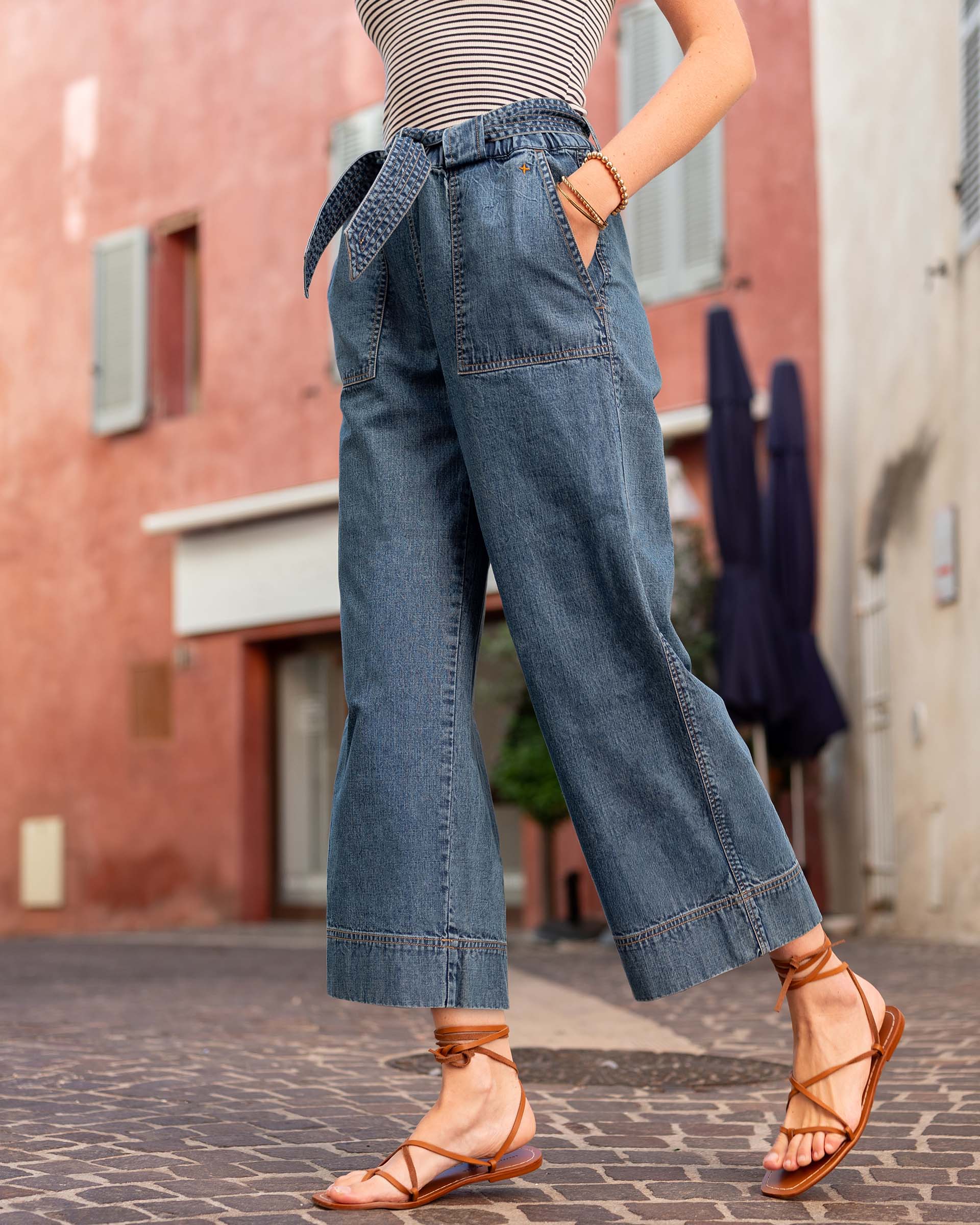 Person wearing blue denim wide-leg pants and brown sandals on a street.