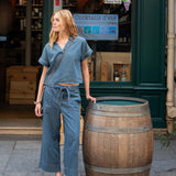 Woman in denim outfit standing next to a wooden barrel in front of a bar.