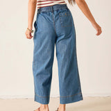 Person wearing blue denim pants and a striped shirt on a plain background