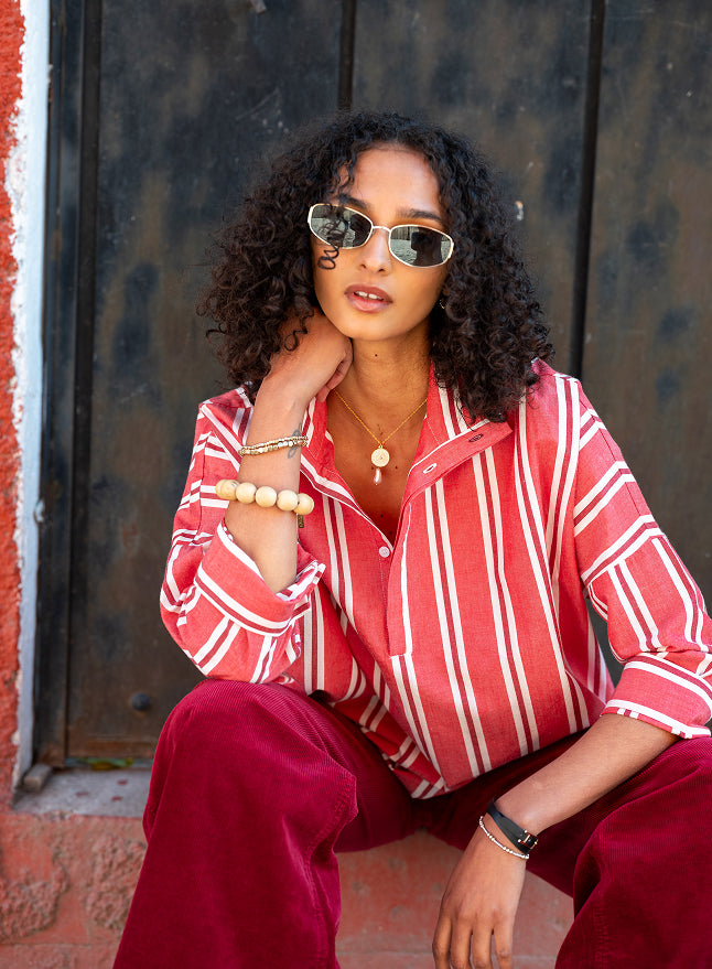 Image of a woman sitting and wearing a red and white striped collared shirt 