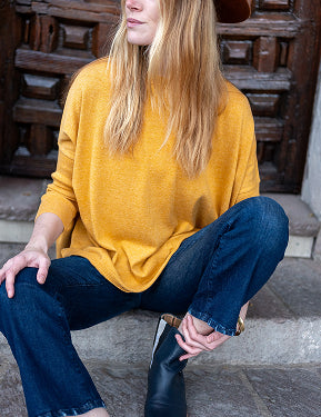 Woman in mustard yellow sweater and blue jeans sitting on steps wearing a brown hat.
