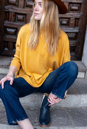 Woman in mustard yellow sweater and blue jeans sitting on steps wearing a brown hat.