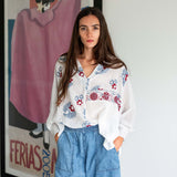 Woman wearing a floral blouse and blue jeans standing in front of a framed poster.