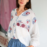Woman wearing a white blouse with floral patterns and blue jeans indoors.