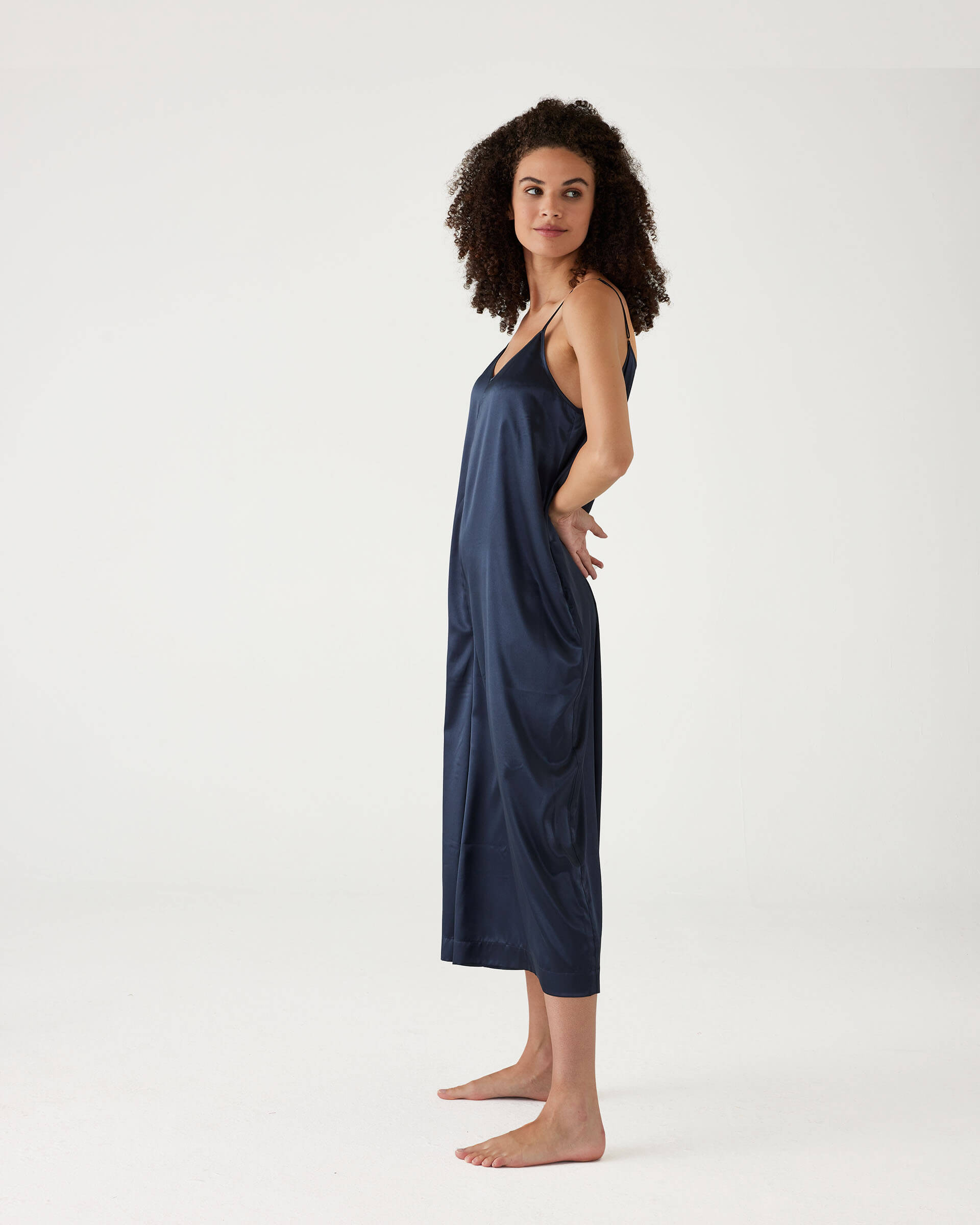 female wearing Mersea garnet satin jumpsuit standing sideways against white background