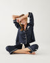female wearing Mersea sapphire satin sailor pajama set sitting cross legged against white background