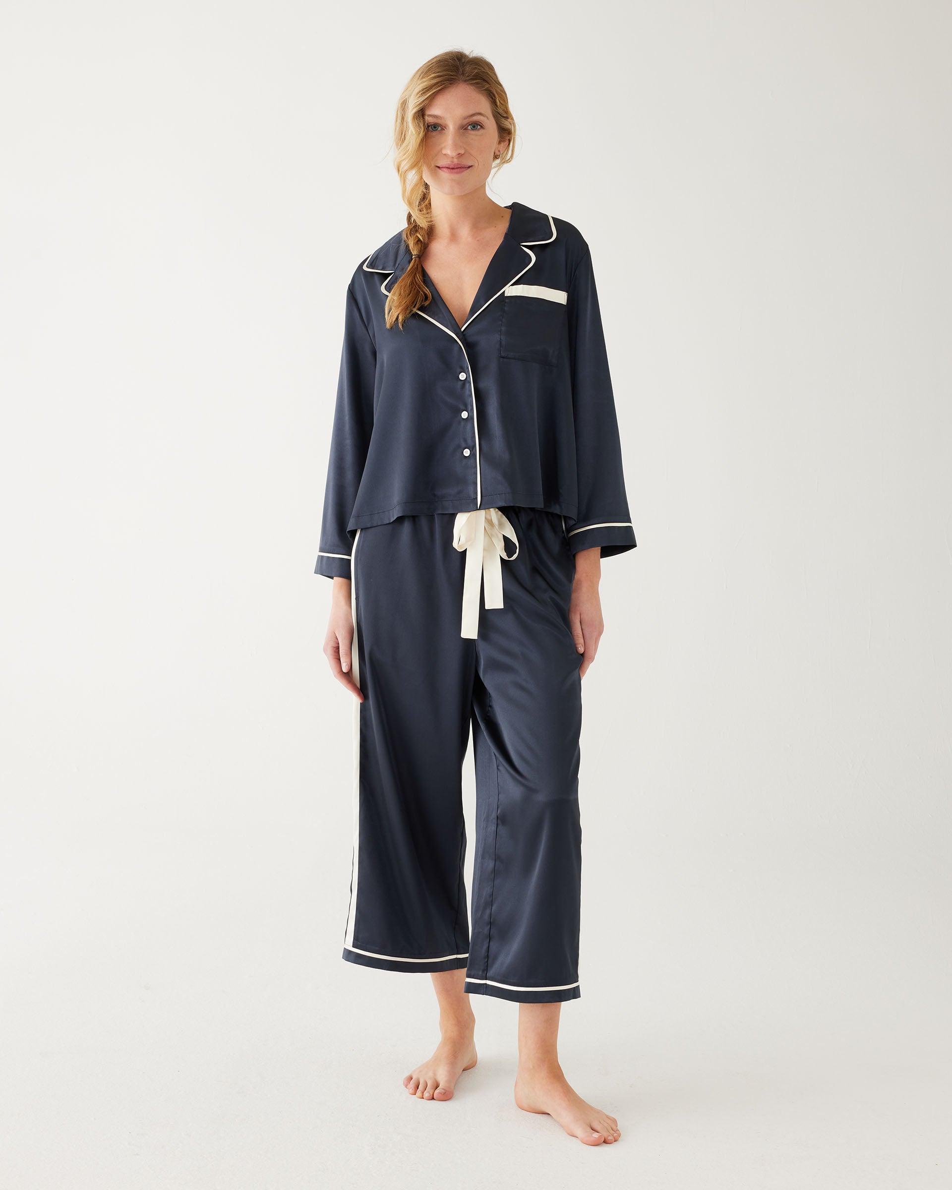 female wearing Mersea sapphire satin sailor pajama set standing against white background
