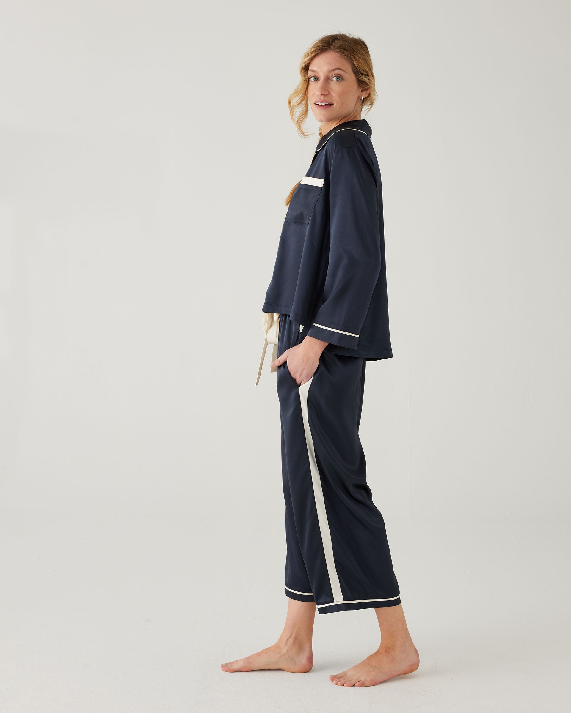 female wearing Mersea sapphire satin sailor pajama set standing sideways against white background