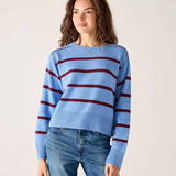 Woman wearing a blue sweater with red stripes and jeans against a plain background