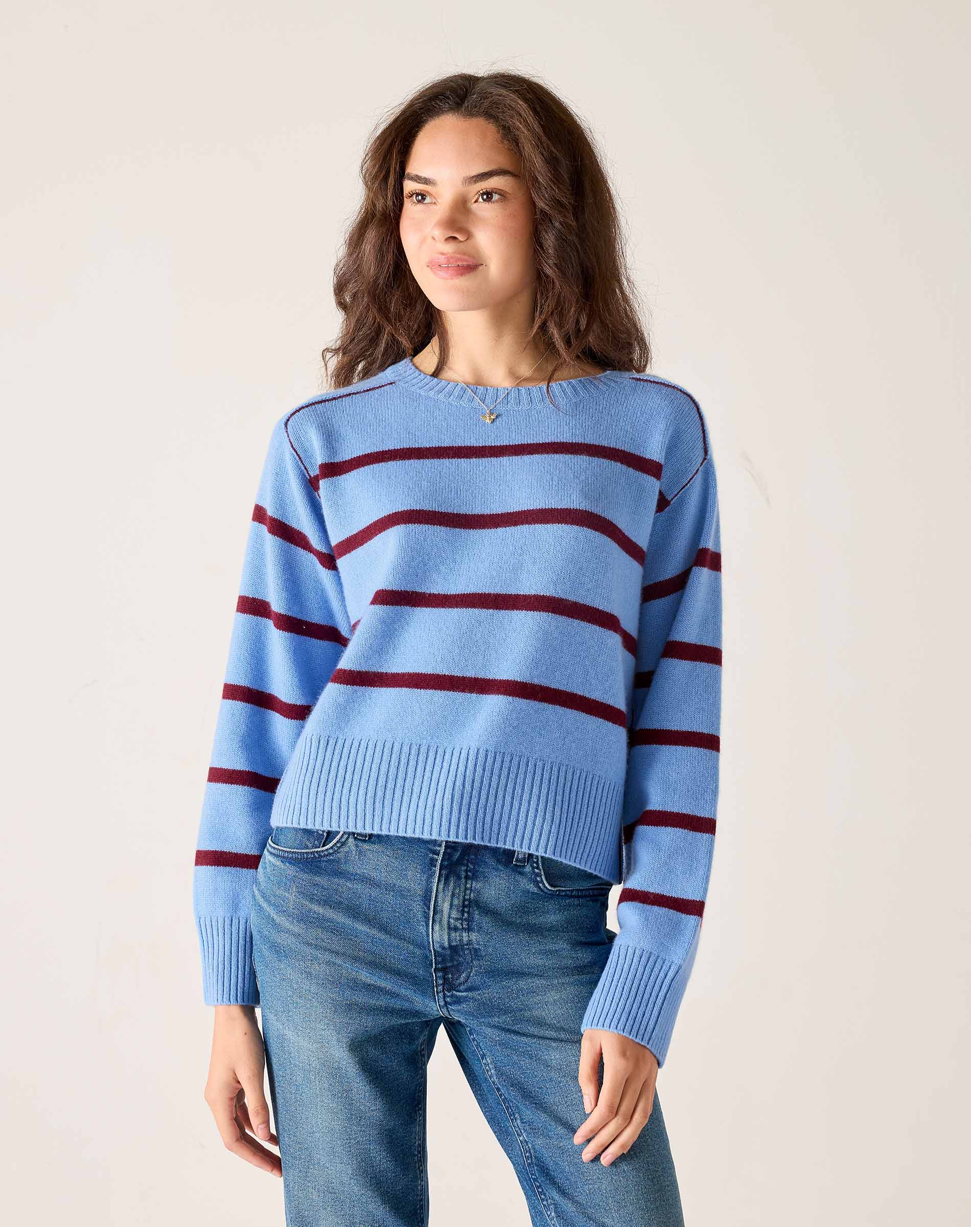 Woman wearing a blue sweater with red stripes and jeans against a plain background