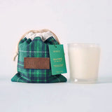 MERSEA women's travel-friendly green and navy plaid drawstring pouch bag and a white candle in a clear glass jar with a green label that reads 'MERSEA SEA PINES'. Text: "MERSEA SEA PINES, SEA PINE SCENT, MERSEYED SOY CANDLE, HAND POURED IN THE USA 10 OZ / .32 OZ""