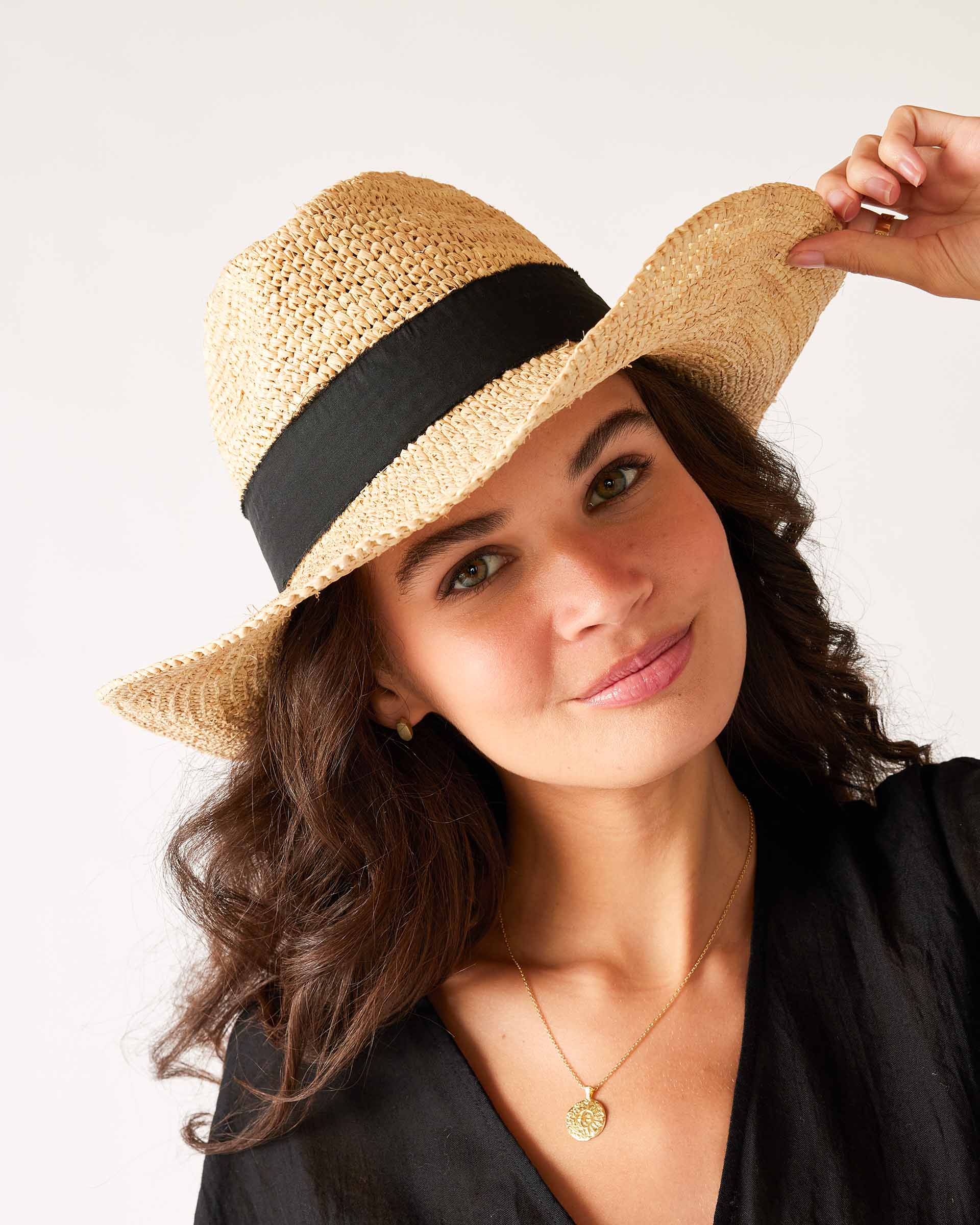 woman in a black dress wearing seagrove straw hat  with hand on brim