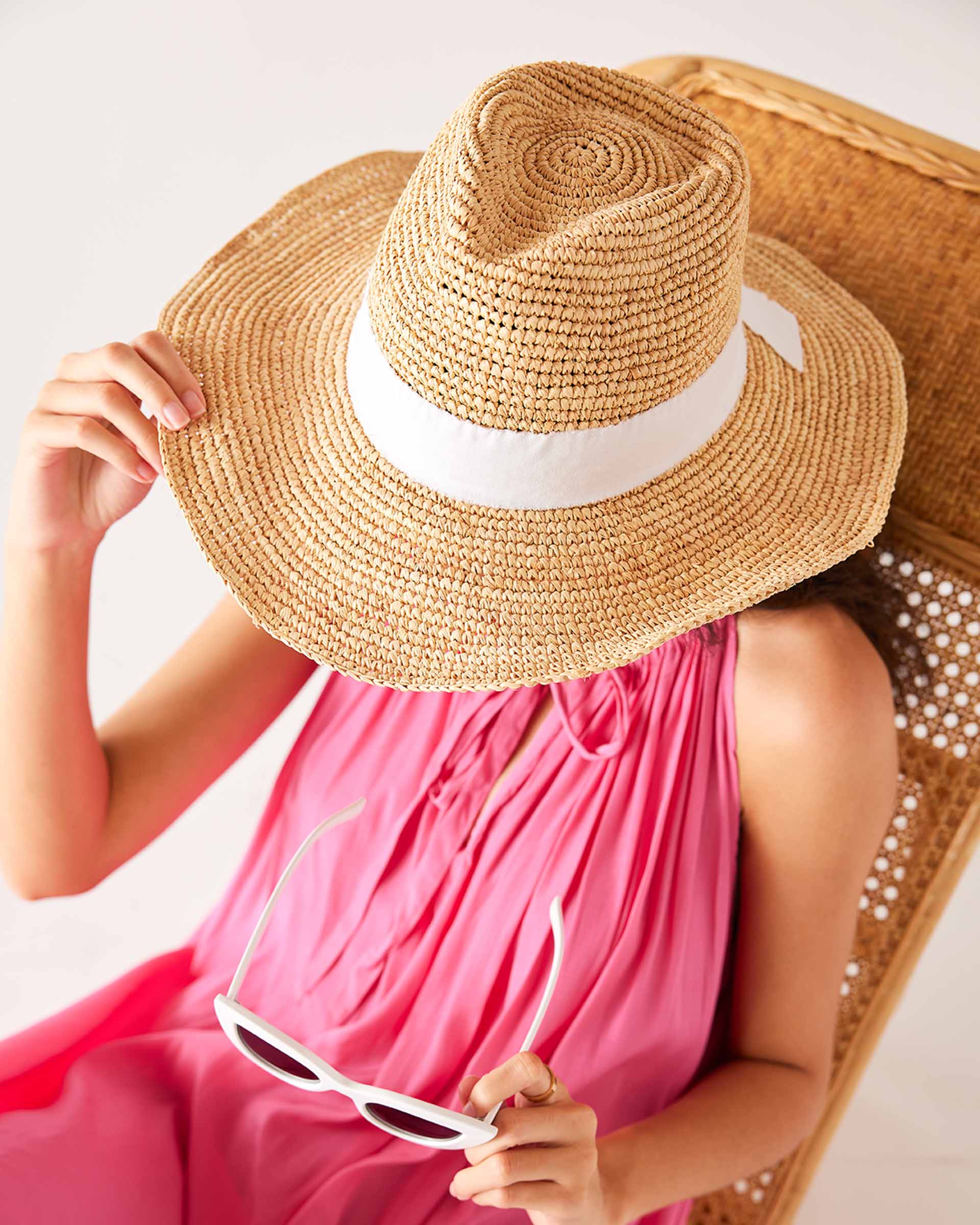 top down shot of woman wearing seagrove straw hat with hand on the brim and sunglasses in hand