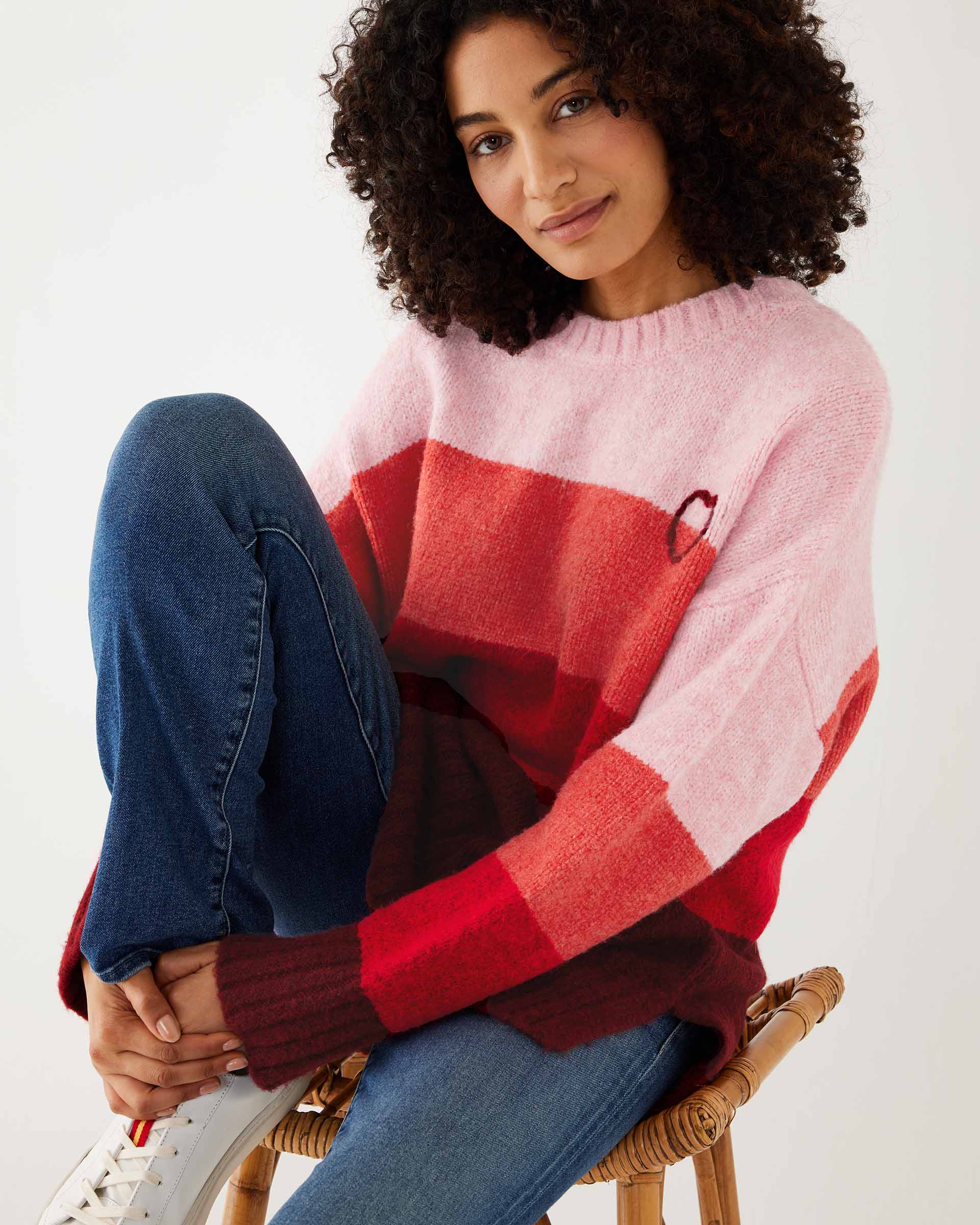 closeup of woman wearing mersea seahappy heart holiday sweater in bliss pink stripes sitting on stool