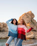 women wearing mersea seahappy heart and peace holiday sweaters in bliss pink stripes and galxy blue stripes on beach