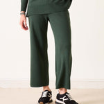 Person wearing a green sweater and pants with black and white sneakers on a light background