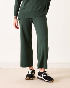Person wearing a green sweater and pants with black and white sneakers on a light background