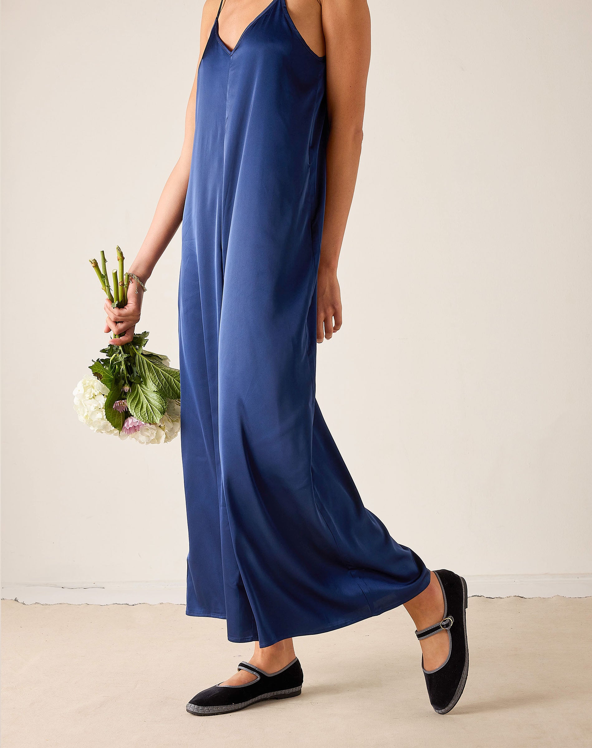 Woman wearing a blue dress holding flowers against a plain background