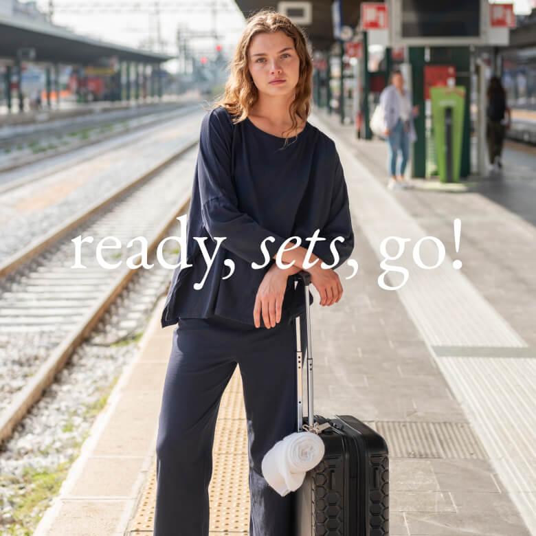 Ready, sets, go! - image of women with a navy travel tee set with a suitcase standing at a train station