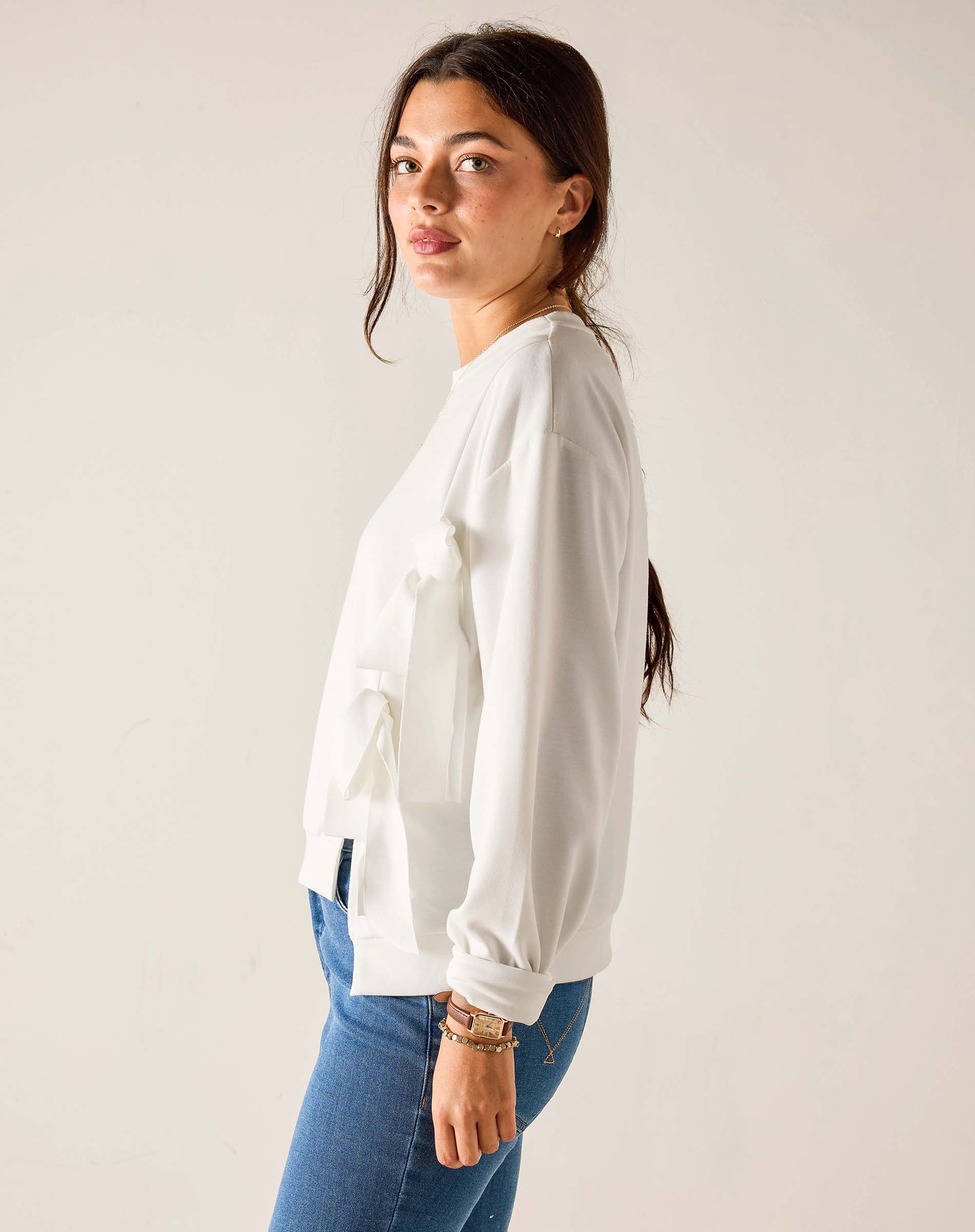 Woman wearing a white blouse and blue jeans against a plain background