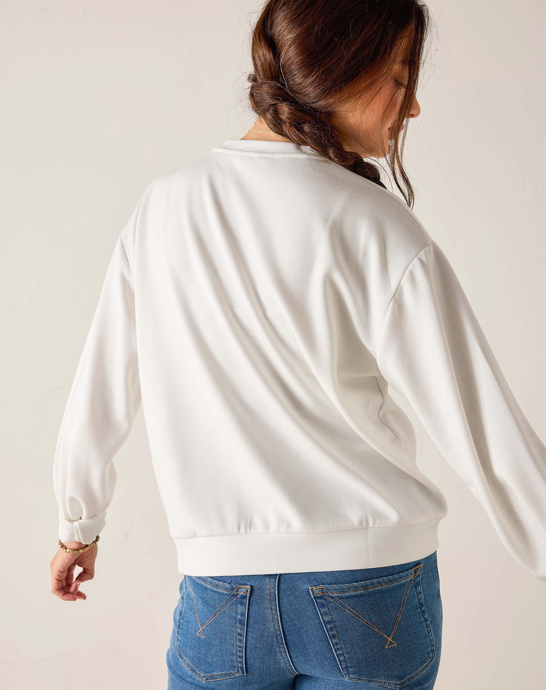 Person wearing a white sweatshirt and blue jeans on a plain background