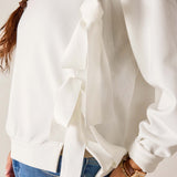 White blouse with ruffled details worn by a person, with a neutral background