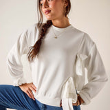 Woman wearing a white blouse with tied sleeves and blue jeans against a plain background