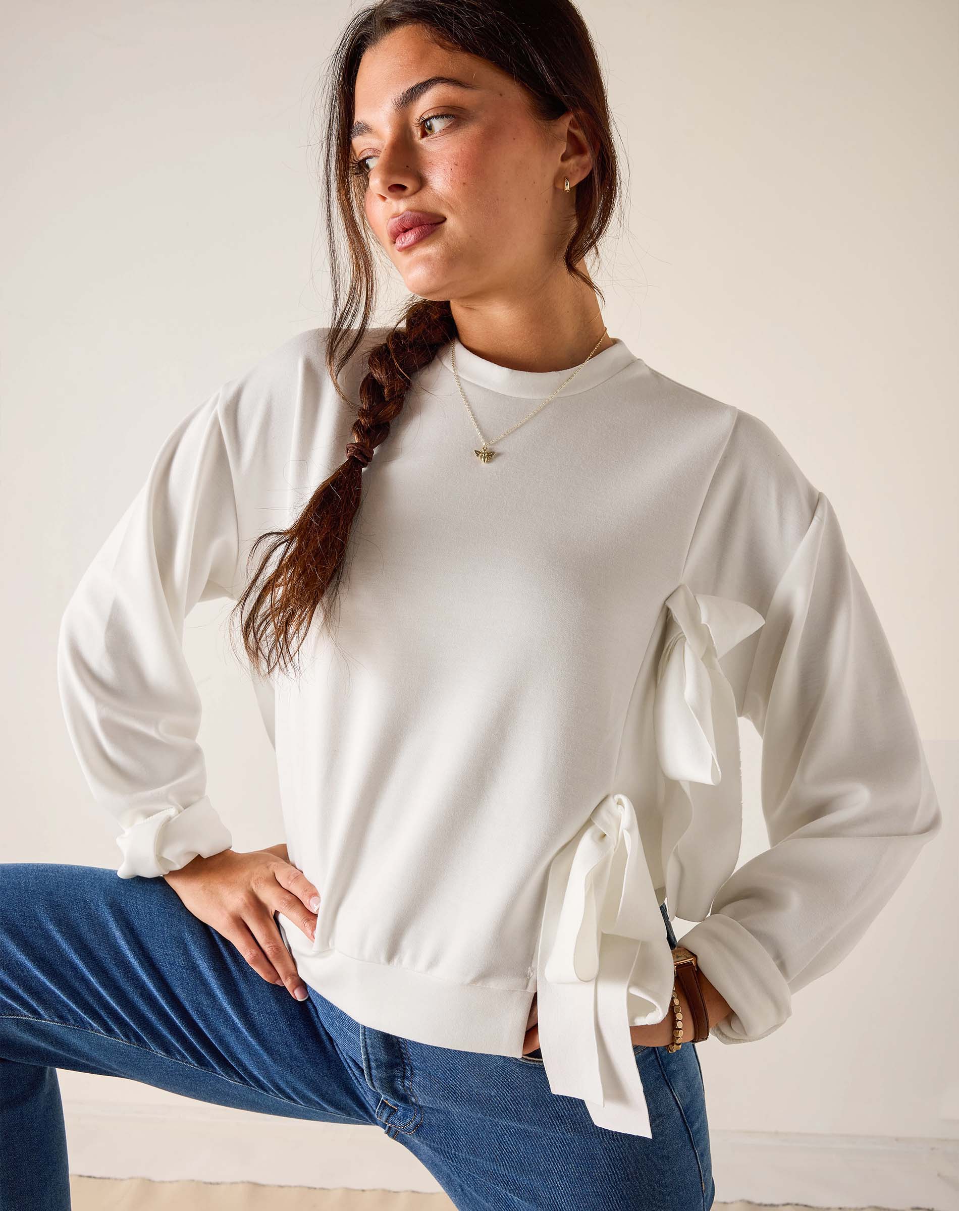 Woman wearing a white blouse with tied sleeves and blue jeans against a plain background