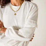 Person wearing a white long-sleeve top with gold jewelry on a plain background