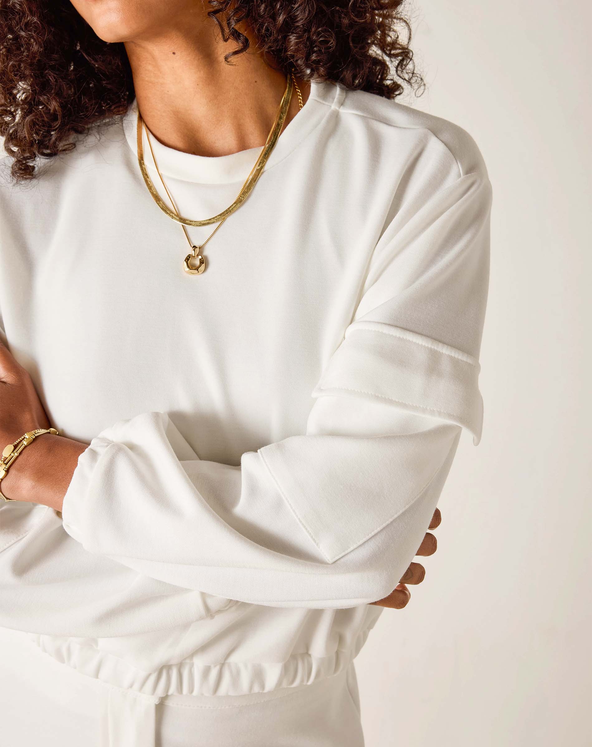 Person wearing a white long-sleeve top with gold jewelry on a plain background