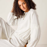 Person wearing a white outfit sitting on a chair with a plain background