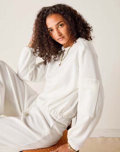 Person wearing a white outfit sitting on a chair with a plain background