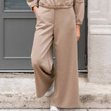 Person wearing a beige tracksuit with wide-leg pants standing on a stone step.