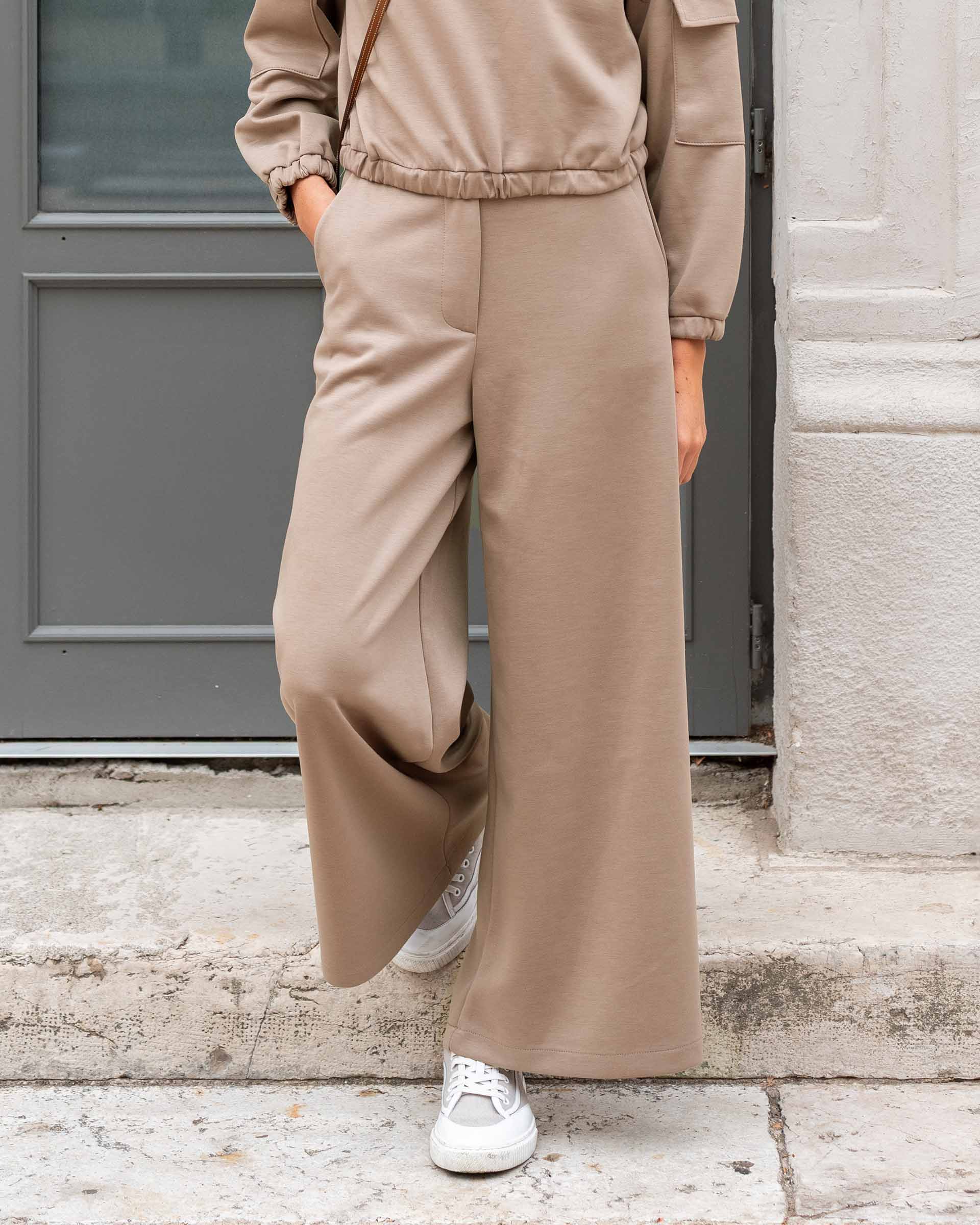 Person wearing a beige tracksuit with wide-leg pants standing on a stone step.