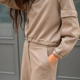 Person wearing a beige tracksuit against a gray background