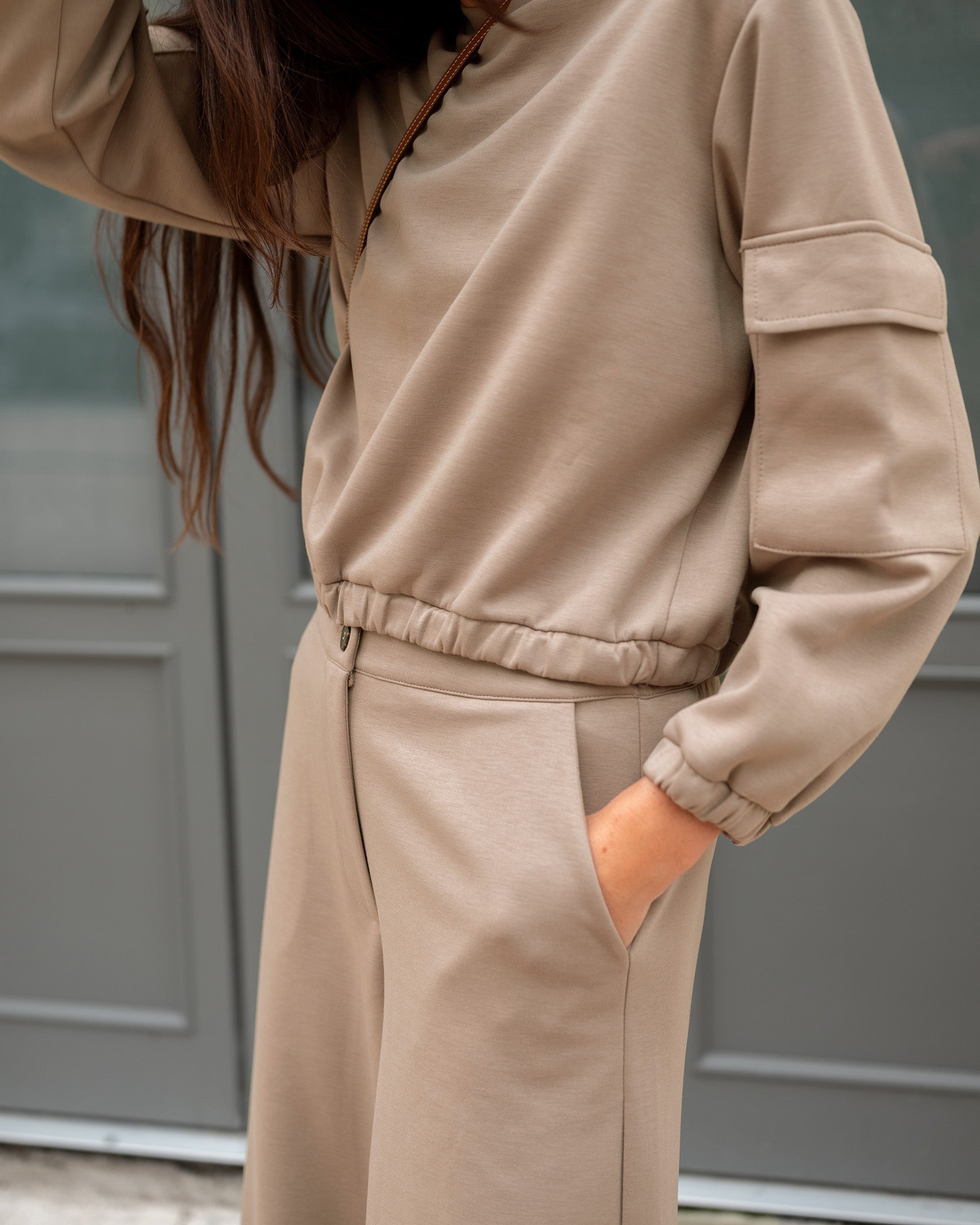 Person wearing a beige tracksuit against a gray background