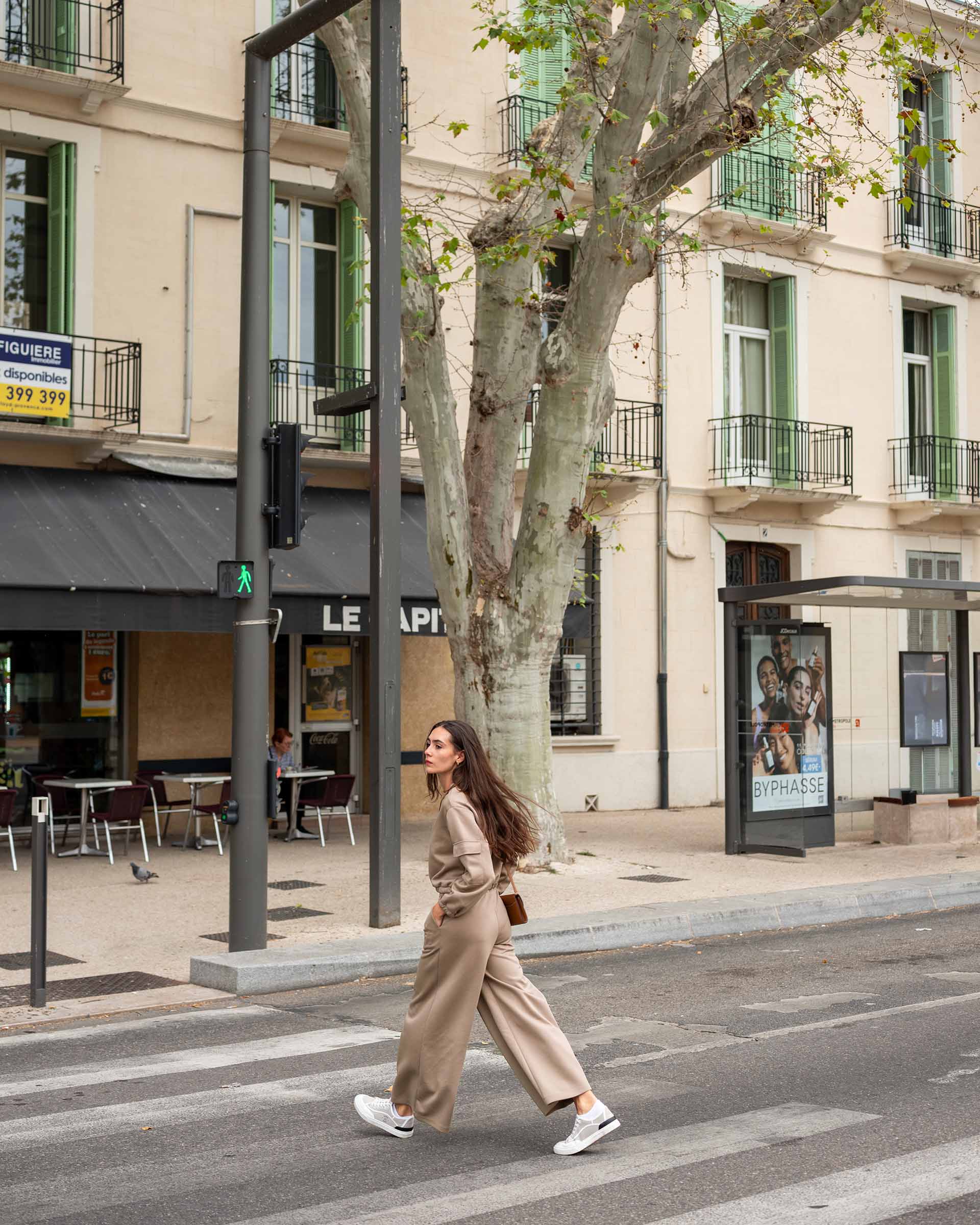 Woman walking on a city street with buildings and trees in the background