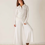 Woman wearing a white knit sweater and wide-leg pants against a plain background