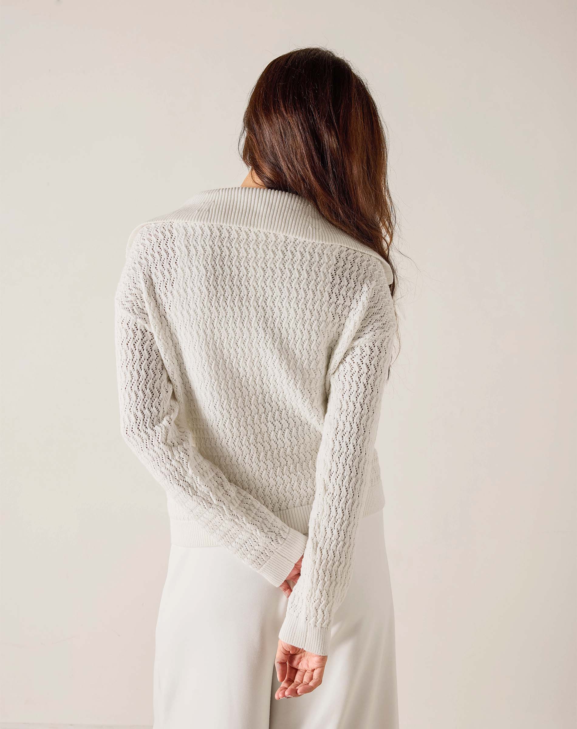 Woman wearing a textured white cardigan against a plain background
