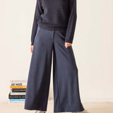 Person wearing a dark sweater and wide-leg pants standing next to books on a light background