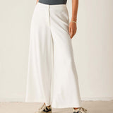 Person wearing white wide-leg pants and a dark top against a plain background