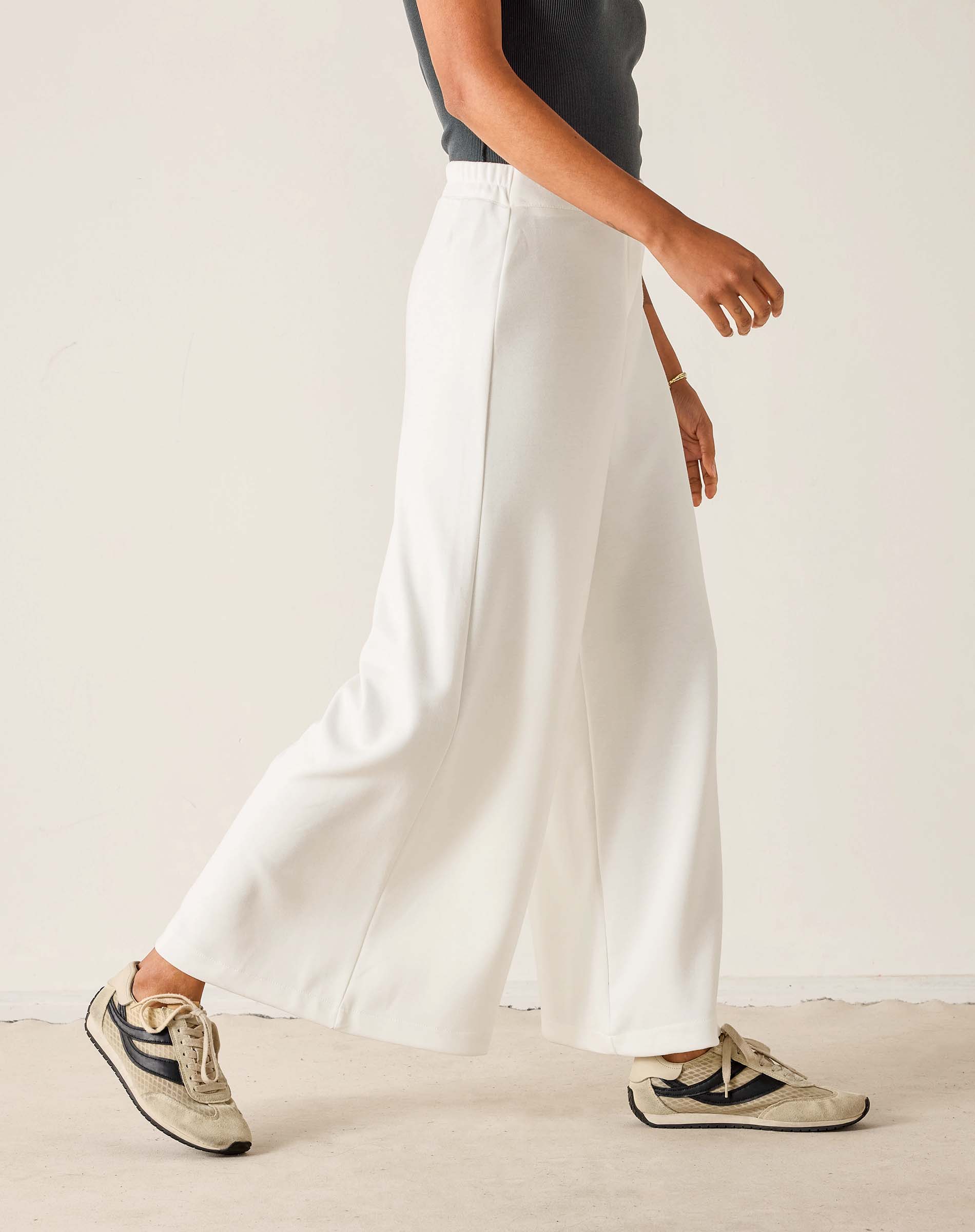 Person wearing white pants and sneakers on a plain background