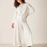 Person wearing a white outfit with wide-leg pants against a plain background
