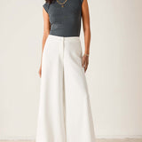 Person wearing a dark gray sleeveless top and white wide-leg pants on a plain background